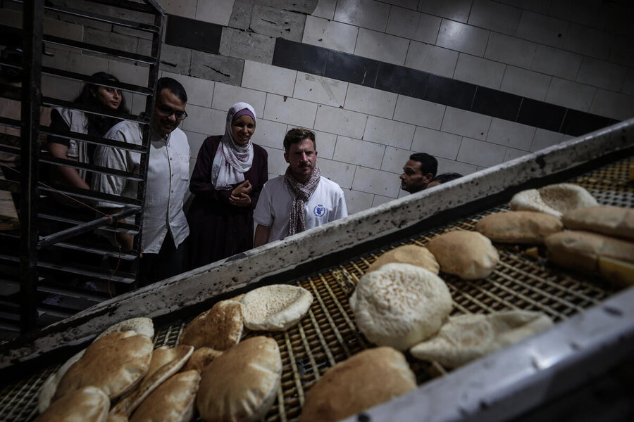 People look on in a bakery at a diagonal round flatbread rolls by on a conveyor belt