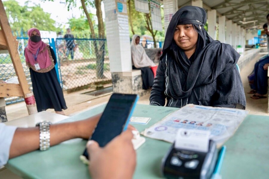 A woman in a black headscarf sits in front of a table to collect food assistance in Cox's Bazar. Photo: WFP/Rawful Alam