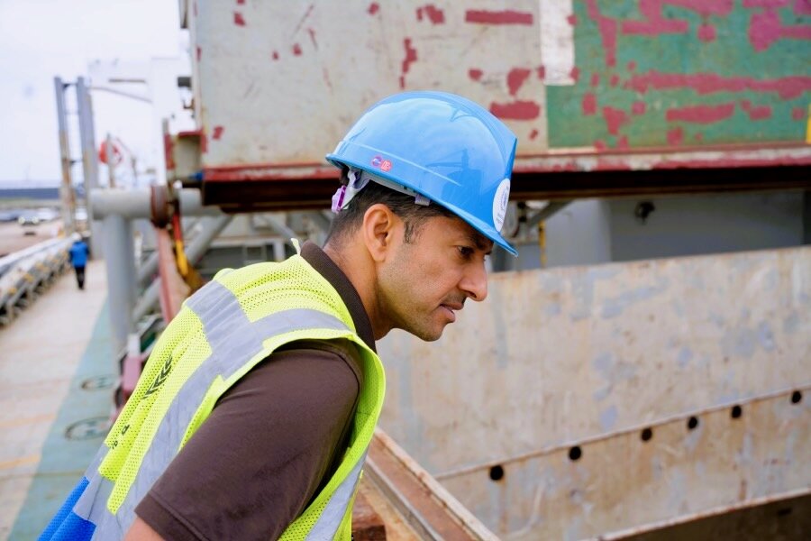 A man in a blue hardhat and yellow WFP jacket stands in front of a cargo vessel at a South Korean port. Photo: WFP/Yanghae Won